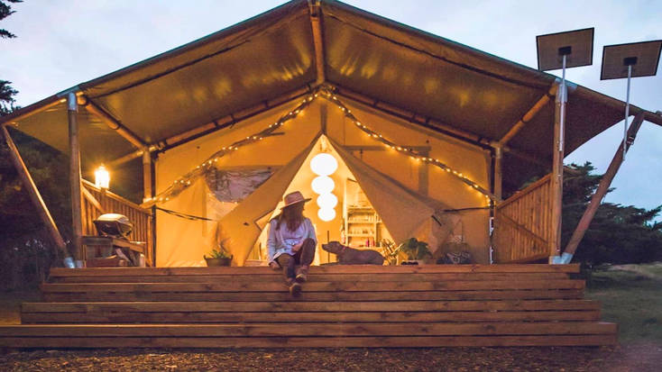 A woman and dog sitting outside a safari tent rental on Phillip Island near Melbourne.