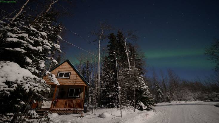 A Glamping Hub cabin at night with the Aurora Borealis in the night sky