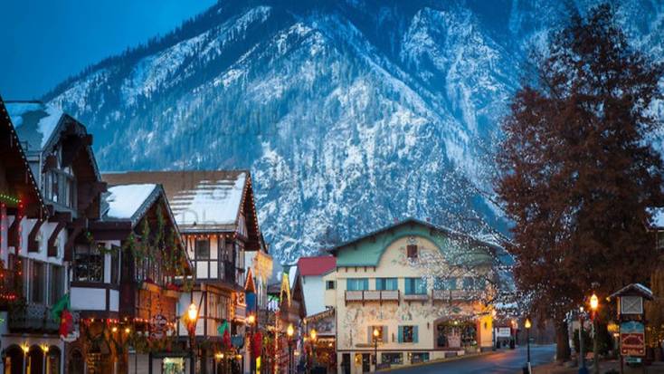 The Bavarian-style town of Leavenworth, WA at dusk with snow-covered rooftops and a mountain in the background