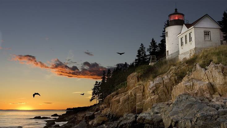 A light house in Maine on a rocky coastline at sun set.
