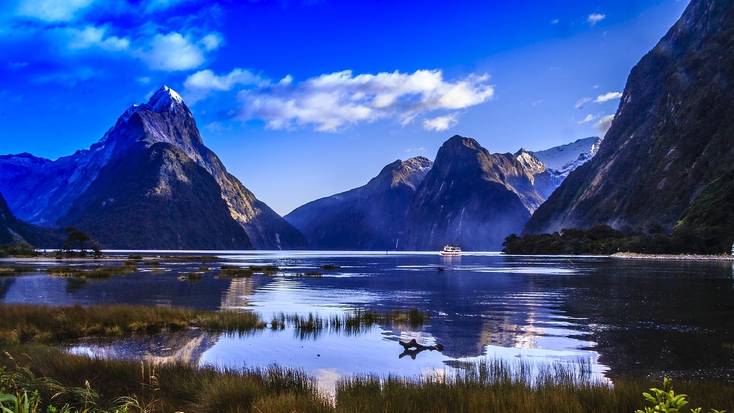 Mountains tower over a lake in New Zealand with a boat on it. 
