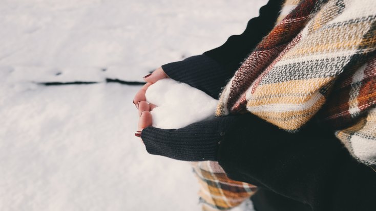 Woman holding ice while glamping in the snow with winter essentials like nourishing hand cream 