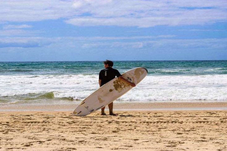 Man standing on beach with surf board on Australia Day 2020, ready for the rest of the day's festivities.
