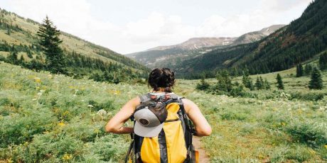 A woman with a yellow hiking pack walking through a green valley.