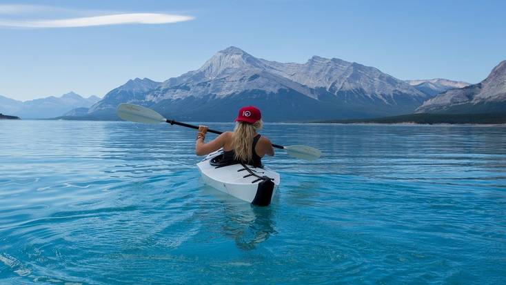 a girl kayaking on a lake with mountains in the background