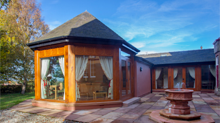 Outside of modern cottage for winter glamping with bay windows and blue skies above. 