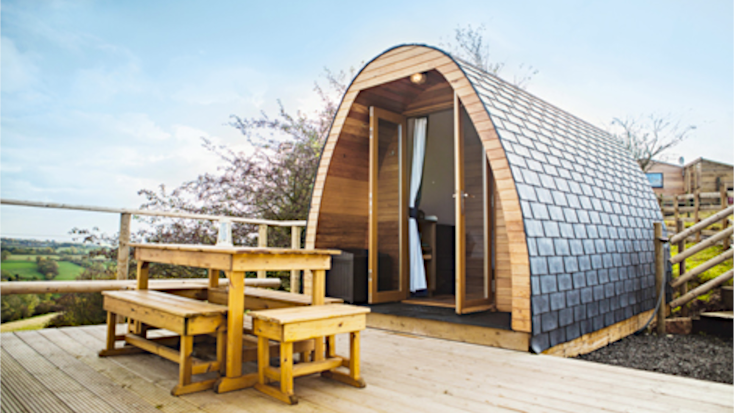 Image of pod rental exterior for eco friendly glamping UK with wood burner outside. 