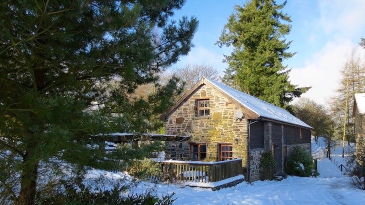 Unique stone cottage exterior with surrounding trees for UK luxury camping. 