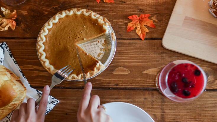 Someone cutting a slice of pumpkin pie for Thanksgiving 2020