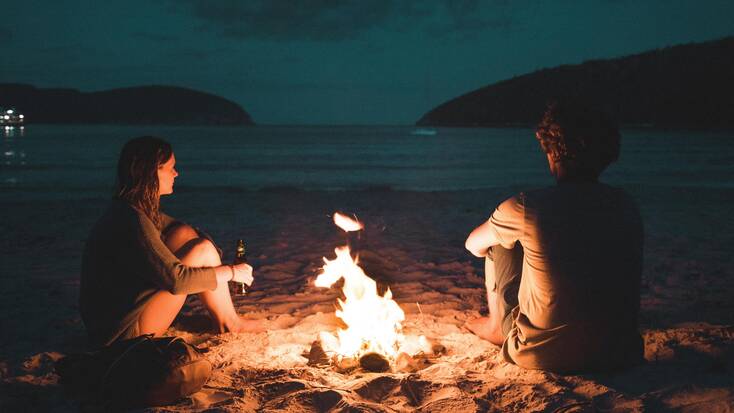 A couple by a bonfire while beach camping