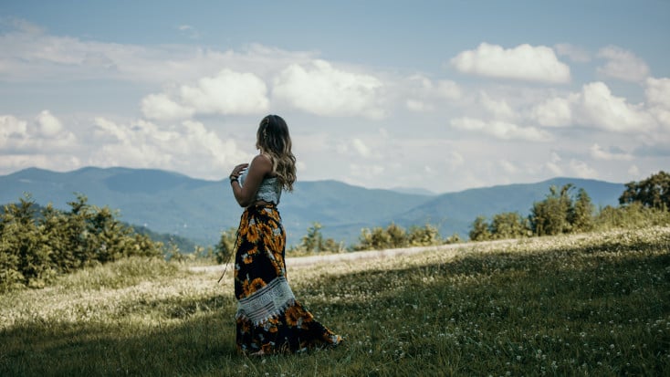 Woman in a field looking at the mountains and the storm clouds