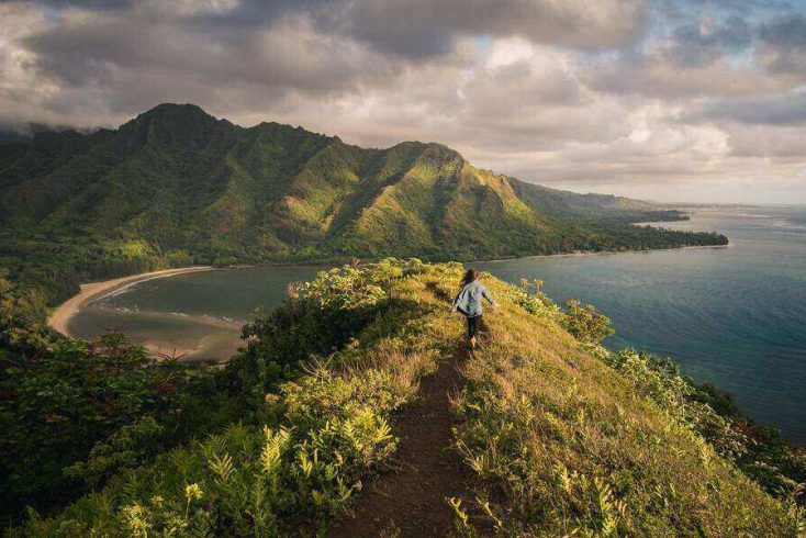 A woman walking over a mountain towards one of the best beaches in Hawaii
