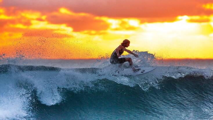 A surfer dude surfing a wave in the sunset