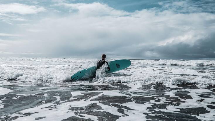 A surfer walking into the ocean in Westport, WA