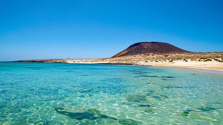 A beach on the canary islands with a volcano ion the background