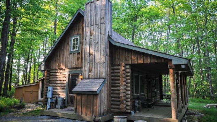 Log cabin with chimney and deck surrounded by woodland in McHenry, Maryland