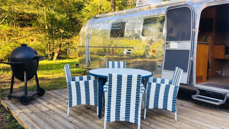 Silver Airstream with deck and outdoor furniture in green and BBQ