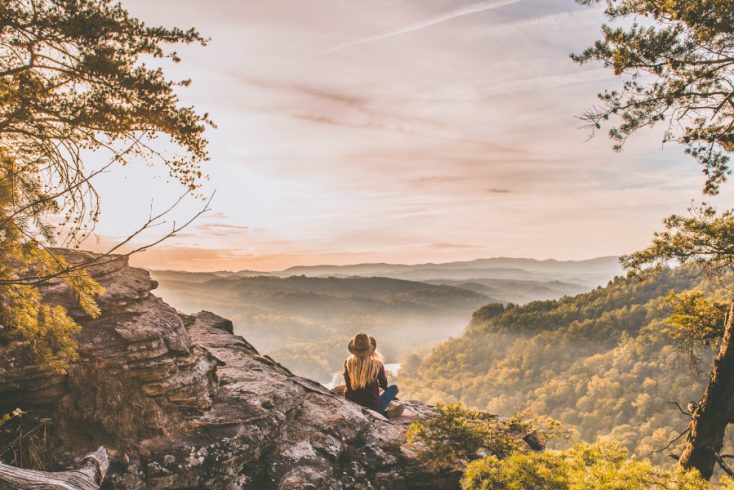 Woman sitting on an outcrop looking at a mountain view at sunrise