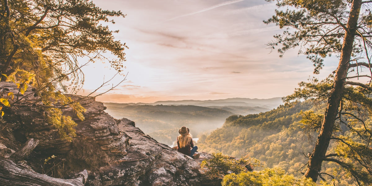 Woman sitting on an outcrop looking at a mountain view at sunrise